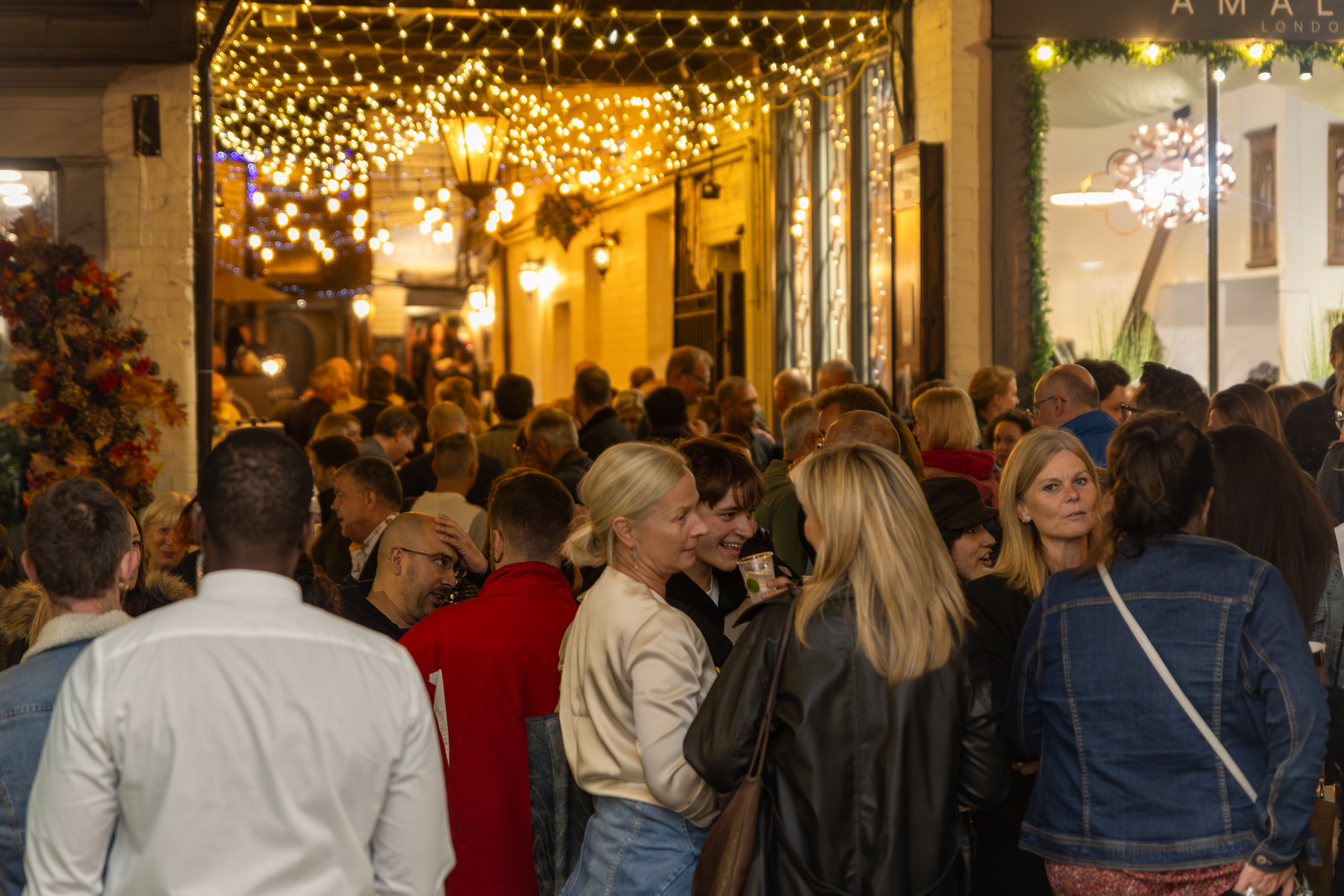 Evening crowds at the Gin and Jazz Festival in St Albans, with warm festoon lights, busy walkways and a lively city-centre atmosphere.